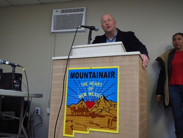Max Gruner, Regional Representative of the New Mexico Economic Development Department, a caucasian male with a shaved head, addresses the Mountainair Town Council from behind a podium on which a sign in the shape of the State of New Mexico proclaims "MOUNTAINAIR THE HEART OF NEW MEXICO.".